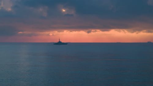 Wide aerial view of a Royal Navy Warship sailing on a calm sea at sunrise.