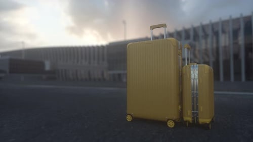 Two yellow suitcases are sitting on the ground in front of a large airport. Concept of travel