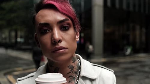 Vista cercana del hombre andrógino mirando a la cámara con un café.