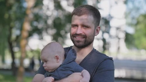 Smiling Father Holding Baby in Park on Sunny Day