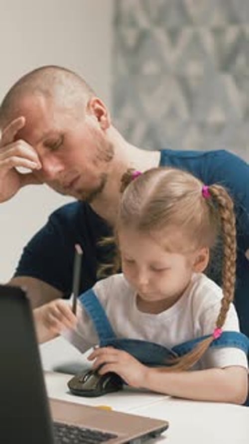 Tired Father Sits at Table with Girl Drawing Computer Mouse