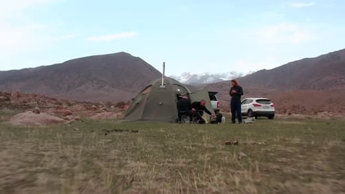 Drone view, tourists gather near tent and cars on mountain valley. Concept of nature holiday.