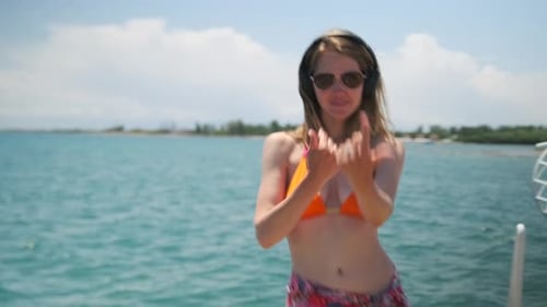 Beautiful blonde dances alluringly on the pier near the sea in headphones and a bright swimsuit