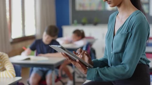 In school, teacher using tablet while students studying in classroom