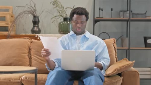 Man Reviews Documents While Working on Laptop at Home