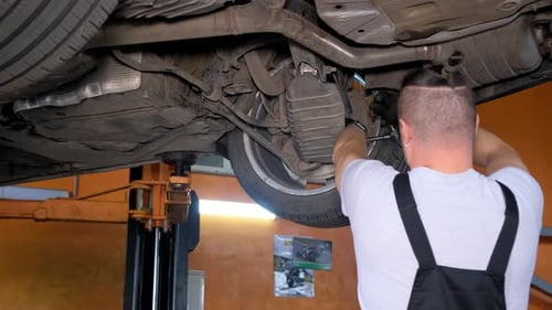 Hipster-Man-Mechaniker arbeitet unter einem Fahrzeug in einer Autowerkstatt