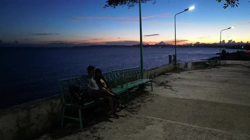 Wide static shot of young romantic couple sitting on a bench with picturesque background view of the