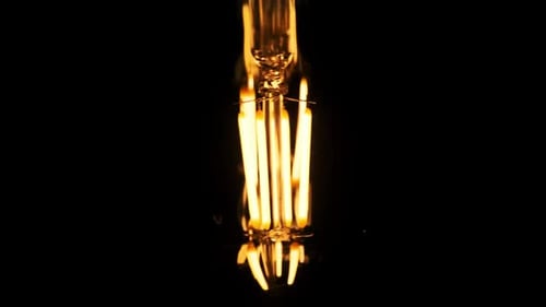 LED-Glühbirne im Retro-Stil, die am Kabel hängt und auf schwarzem Hintergrund flackert