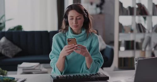 Woman using phone at desk with keyboard and laptop