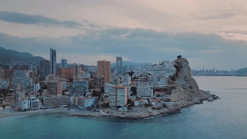 Coastal city with modern buildings on a rocky terrain at golden pink sunset. Modern seafront town.
