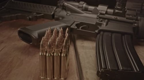 High angle dolly in towards loaded AR-15 assault rifle with a small amount of ammunition in the fore