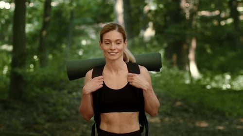 Woman Hiking in the Forest With a Backpack and Yoga Mat on a Sunny Day