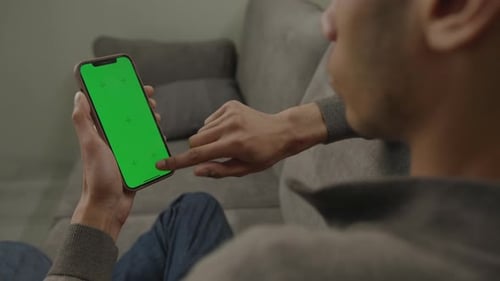 Black Man Using Mobile Phone Green Screen Vertically Sitting on Couch 20s Male Browsing Vertical