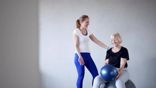 Instructor assisting senior woman exercising with fitness ball