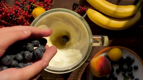 Top View of Children's Hands Throwing Blueberries Into a Mixing Milkshake with Fruits and Berries