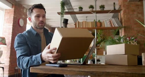 Man Checks Box, Types on Laptop in Home Office