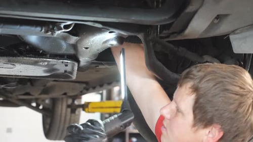 Auto Mechanic Inspecting Bottom and Suspension of a Car at Garage Professional Repairman Working