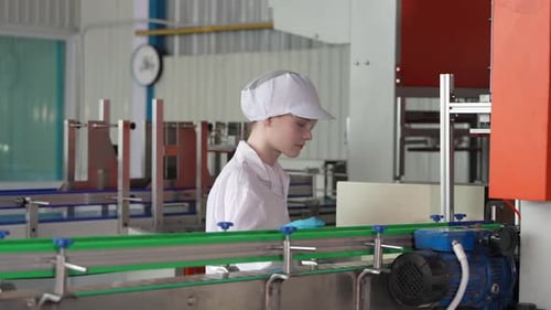 Jeune travailleuse heureuse dans une usine d'embouteillage vérifiant les bouteilles d'eau avant expédition. Qua d'inspection