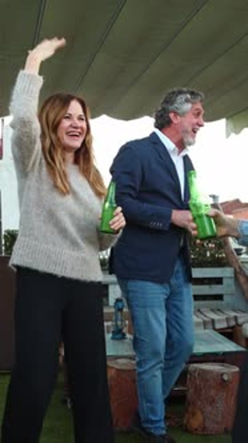 Des amis d'âge mûr dansent et font tinter des bouteilles de bière lors d'une fête en plein air