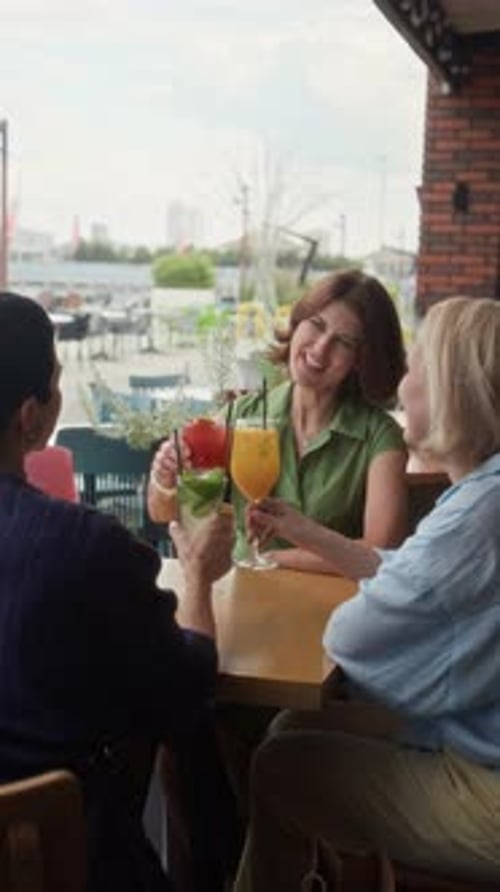 Three Mature Women Clinking Glasses with Cocktails at Outdoor Cafe Table