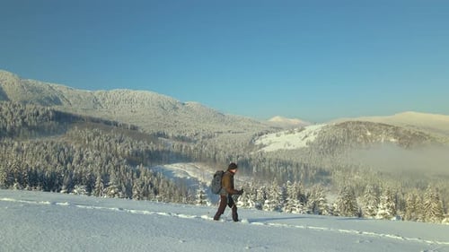 Aerial View of Backpacker Hiking Snowy Mountain Hillside on Cold Winter Day