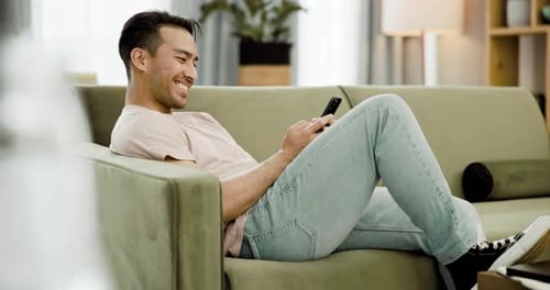 Young Adult Relaxing on Sofa with Mobile Phone