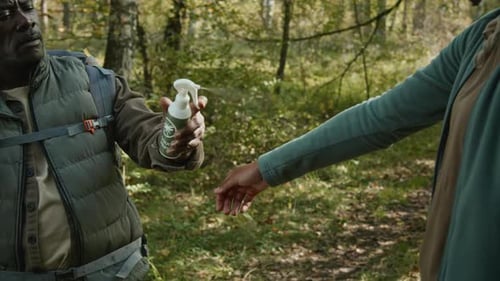 Father Spraying Insect Repellent on Daughters Hiking Clothes on Forest Path