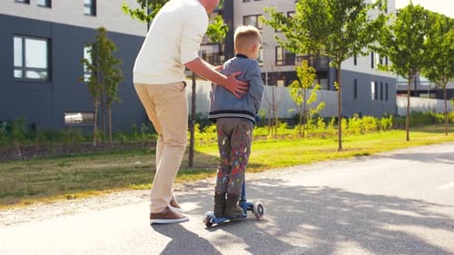 Un père heureux passe du temps de qualité à faire du scooter avec son petit fils dans le parc de la ville