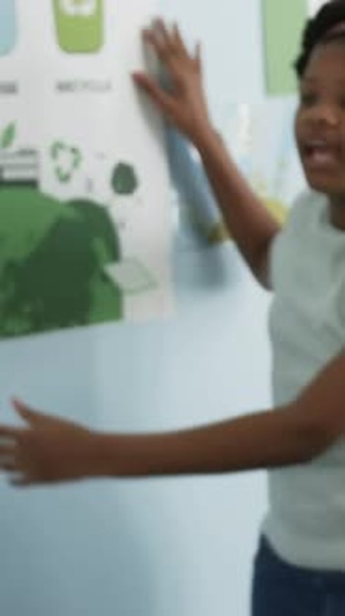 Vertical video: Shifting, student in mint tee pointing at school recycling posters, explaining why