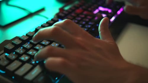 Young gamer plays a video game or typing on colorful keyboard, close up