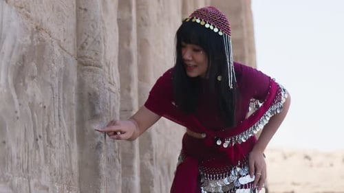 Mujer vestida con un traje tradicional rojo interactuando alegremente con la pared del antiguo templo en Dendera, Egipto