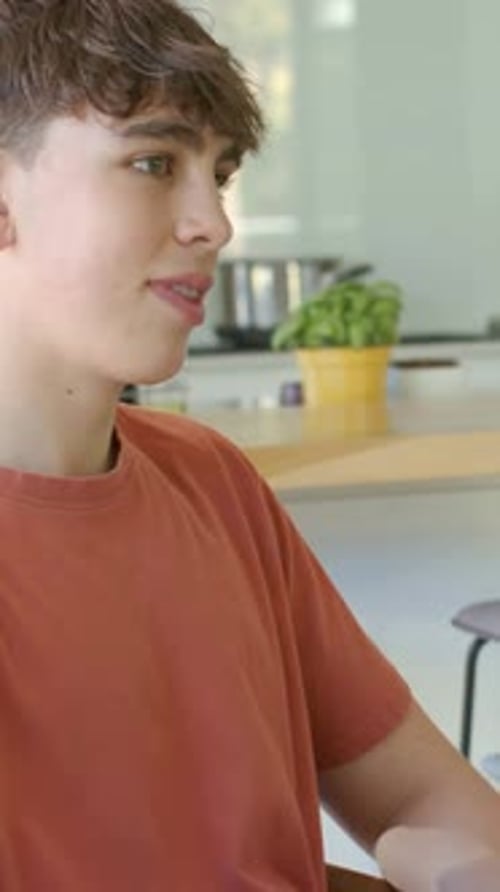 Vertical video: Hearing friend speaking, teen male gesturing, adjusting watch at kitchen, rust tee