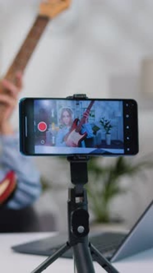 Woman Records Guitar Tutorial on Mobile Phone Indoors