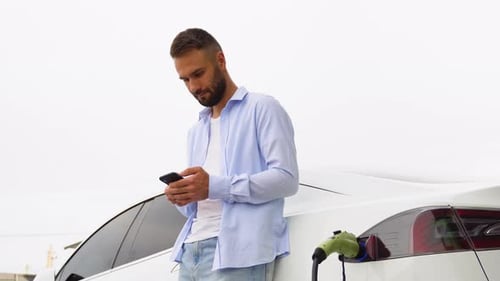 Man Using Phone While Charging Electric Car