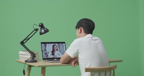 Asian Male Waving Hand For Greeting And Speaking While Studying On Zoom By A Laptop On Green Screen