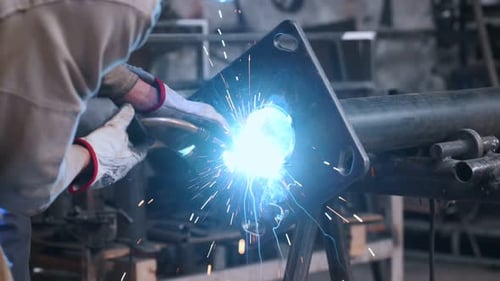 Der Schweißer, der in der Fabrik arbeitet, sammelt ein Metallteil. Zusammenarbeit mit der Stahlindustrie