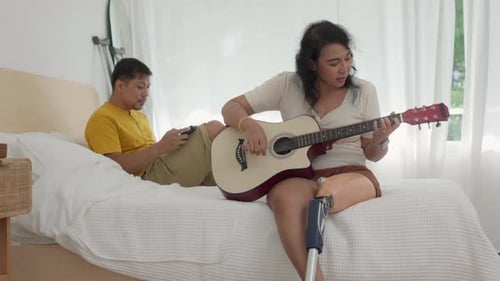 Woman Plays Guitar on Bed While Man Uses Device