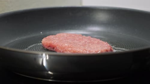 A man cooks burger meat on a hot pan with oil without using a holder. Close up shot, side view of me