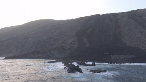 Dramatic White Waves Smashing Rocky Volcanic Shoreline Exposing Rugged Coastal Terrain with