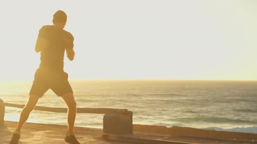 Determined Sportsman Air Boxing on Platform By Sea During Bright Sunset