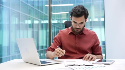 Confident businessman signing documents sitting at a desk at workplace in a business office.