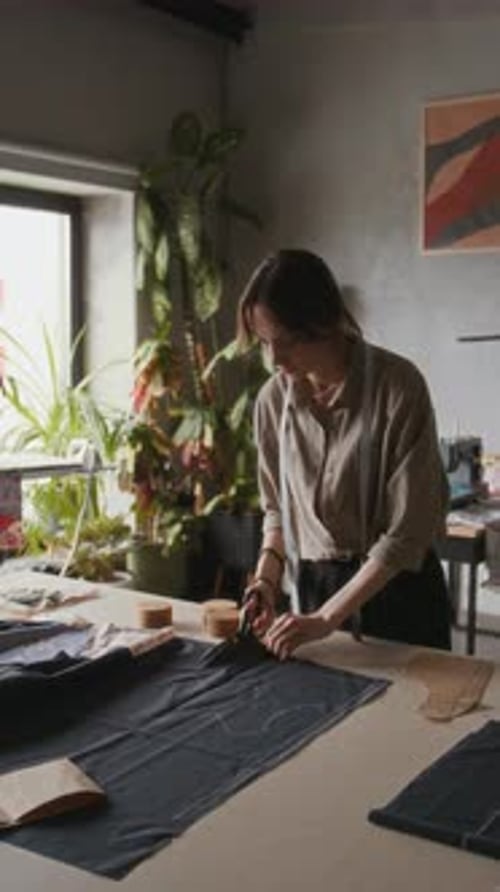 Busy Young Female Tailor Cutting Pattern from Black Fabric in Workshop