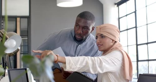 Collaborating in office, holding documents and tablet, colleagues discussing project
