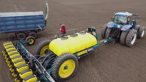 Blue tractor with yellow seeder working on the field in Ukraine OA