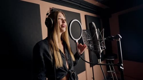 girl singer singing in a recording studio with headphones in front of microphone to create a song