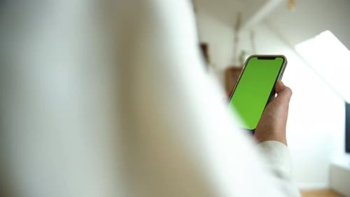 Side view of a causal dressed man holding smartphone with green screen chroma key in white home back