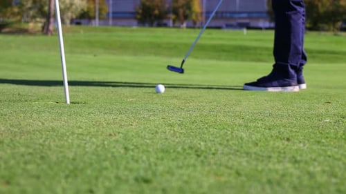 Senior golfer putting ball into hole on green close-up