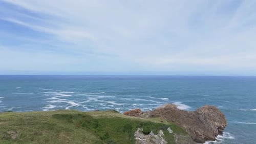 Ascending drone view of calm Cantabrian coast with cirrus clouds and red cliffs