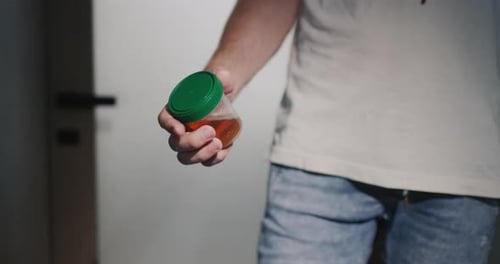 Um homem está na porta do banheiro com um frasco para exames de urina