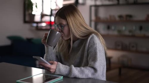 Woman Uses Cell Phone and Drinks Coffee Indoors